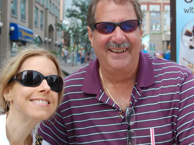 Front this man and this woman wore goggles. Background it is blur. We can see trees, buildings and...