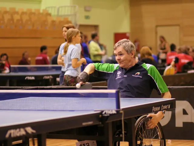 A man who is sitting on the wheelchair is playing table tennis with his hand. In the background we...